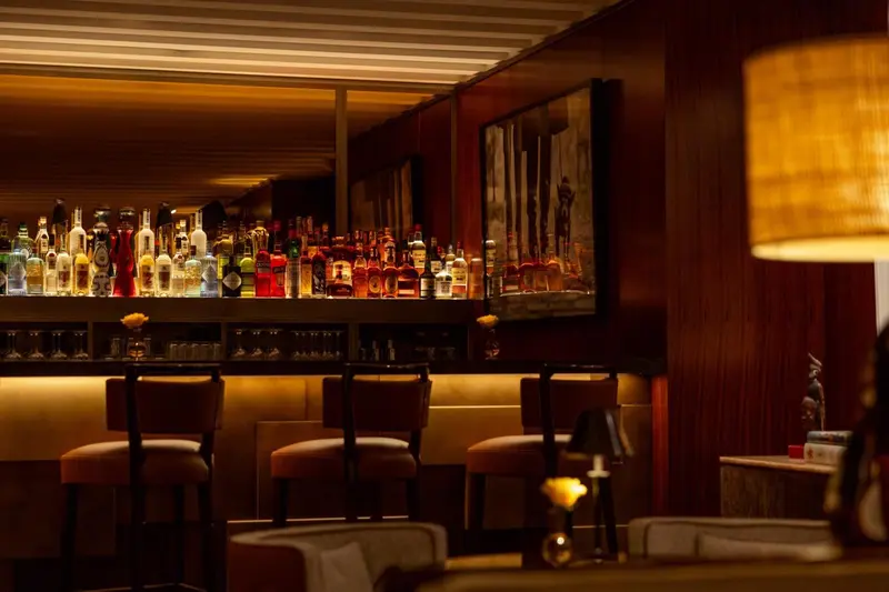 Un comptoir de bar avec des tabourets et des bouteilles éclairées.