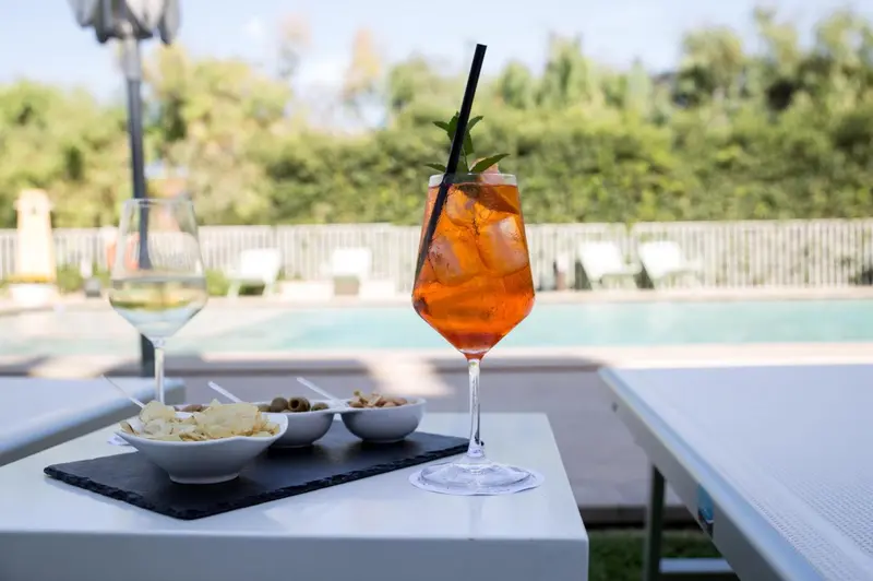 Deux verres et une assiette de collations sont posés sur une table blanche près d'une piscine.