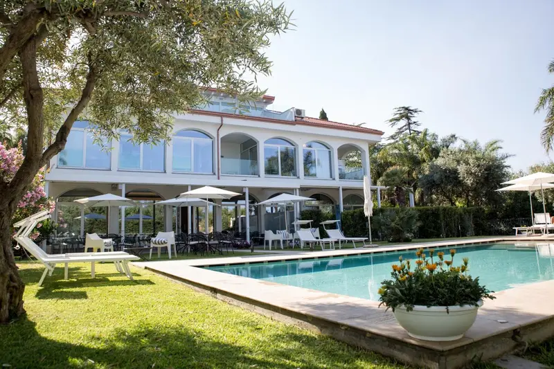 Bâtiment blanc avec arcades donnant sur une piscine et un jardin verdoyant.