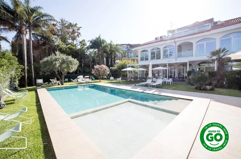 Une piscine rectangulaire bordée de transats dans un jardin soigné.