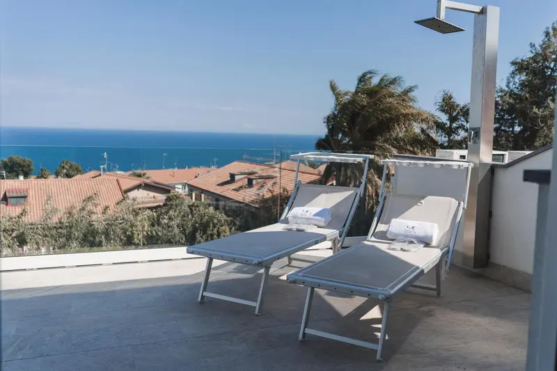 Deux transats blancs sur une terrasse avec vue sur la mer et la végétation.