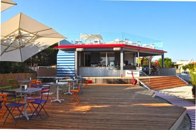 Terrasse en bois avec tables et chaises colorées devant un bâtiment bas.