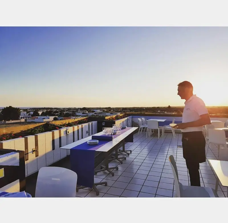 Une terrasse avec des tables et des chaises offre une vue sur la ville au coucher du soleil.