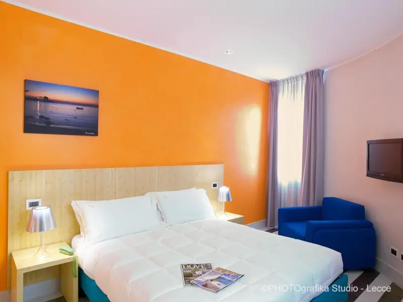 Une chambre lumineuse avec un grand lit et un fauteuil bleu.