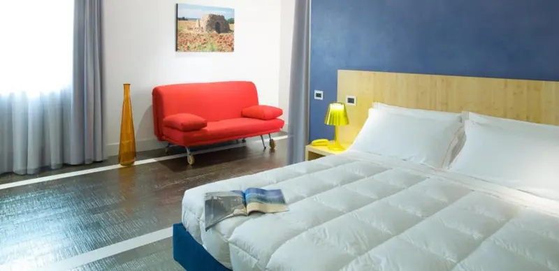 Une chambre lumineuse avec un canapé rouge et un grand lit blanc.