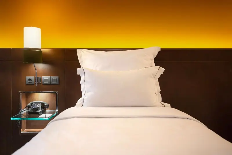 Un lit simple avec oreillers blancs dans une chambre aux murs bruns.