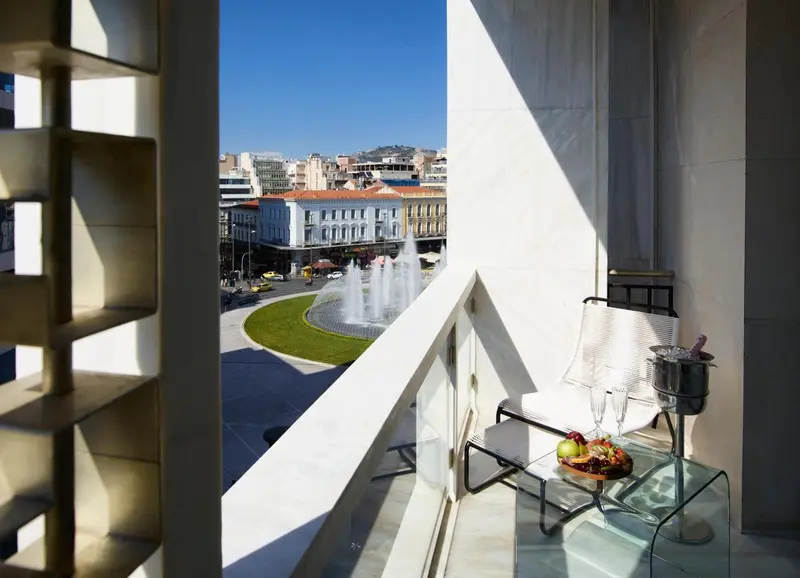 Vue sur une place animée depuis un balcon avec une table et des fruits.