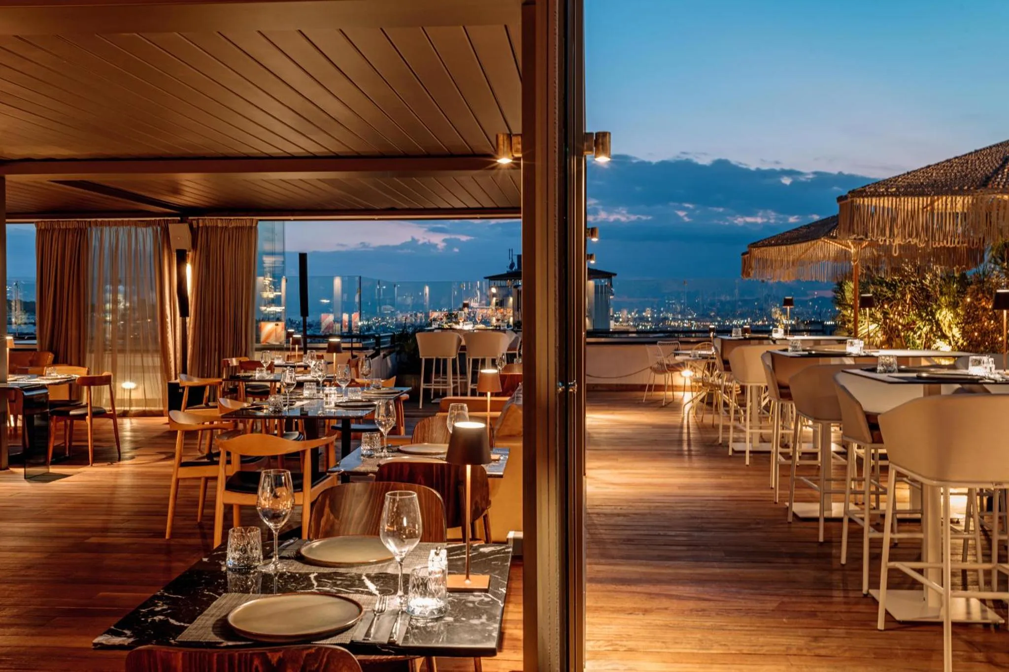 Terrasse de restaurant avec vue sur la ville illuminée au crépuscule.