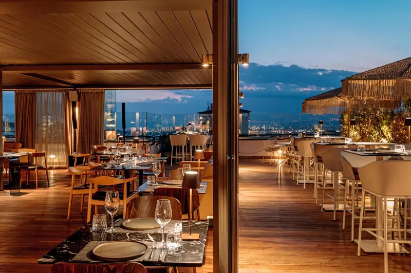 Terrasse de restaurant avec vue sur la ville illuminée au crépuscule.