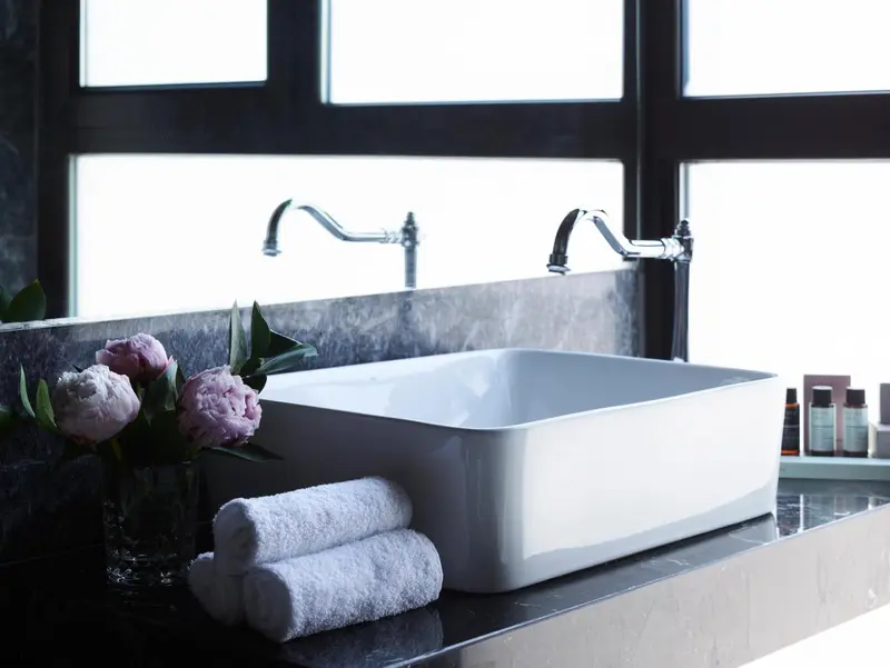 Un lavabo blanc sur un comptoir sombre, avec des serviettes et des fleurs.