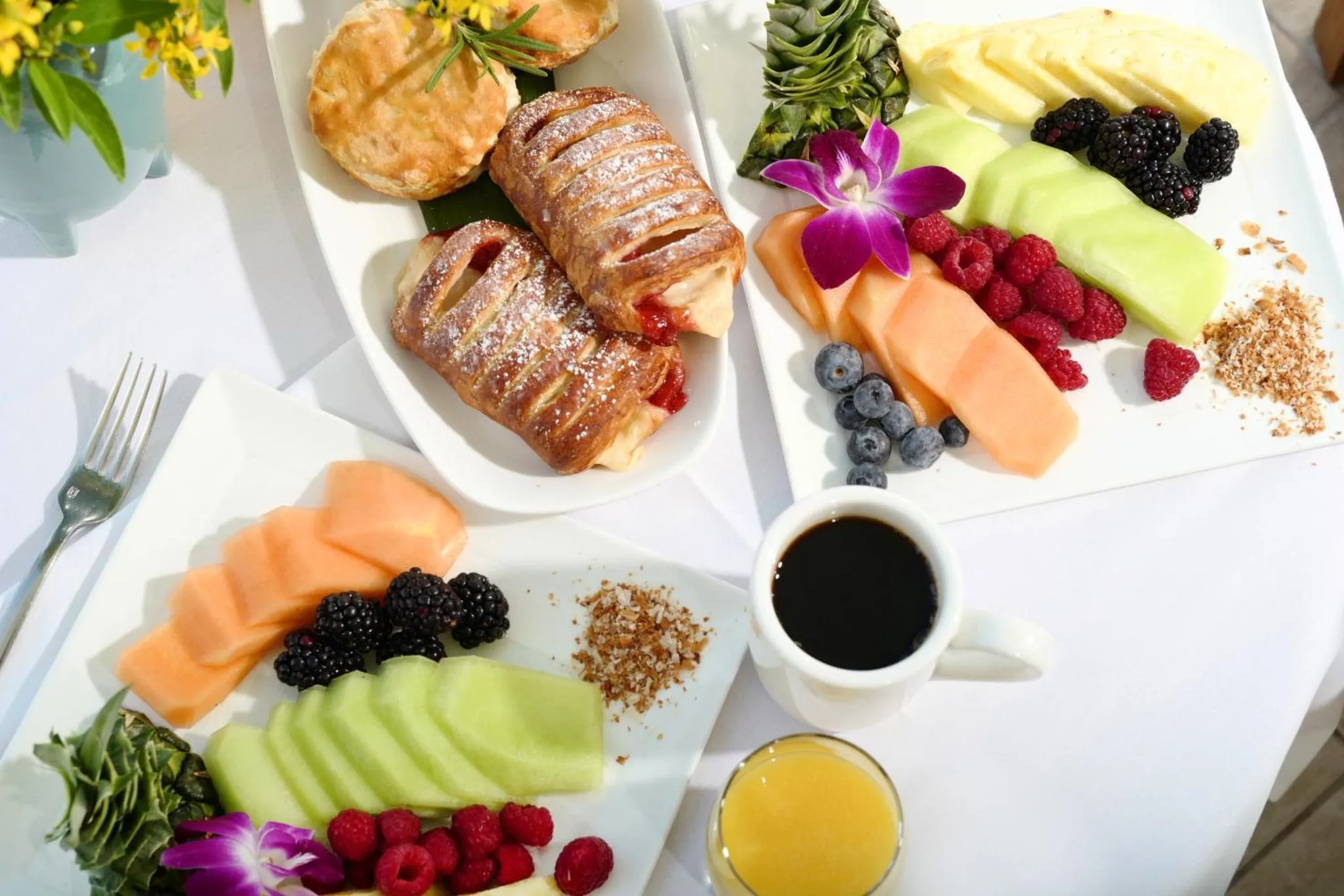 Assiette de viennoiseries, de fruits frais et de jus d'orange sur une table blanche.