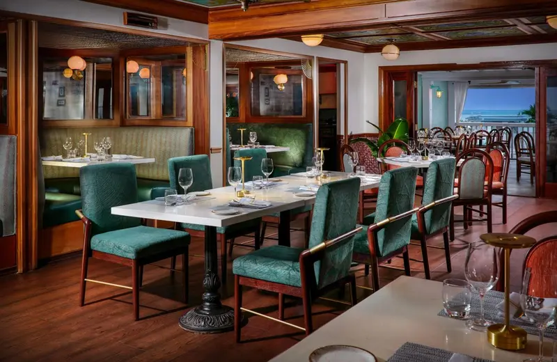 Une salle de restaurant lumineuse avec des tables dressées et des banquettes vertes.
