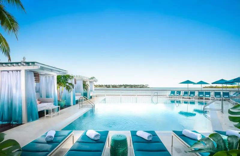 Transats bleus au bord d'une piscine rectangulaire avec vue sur la mer.