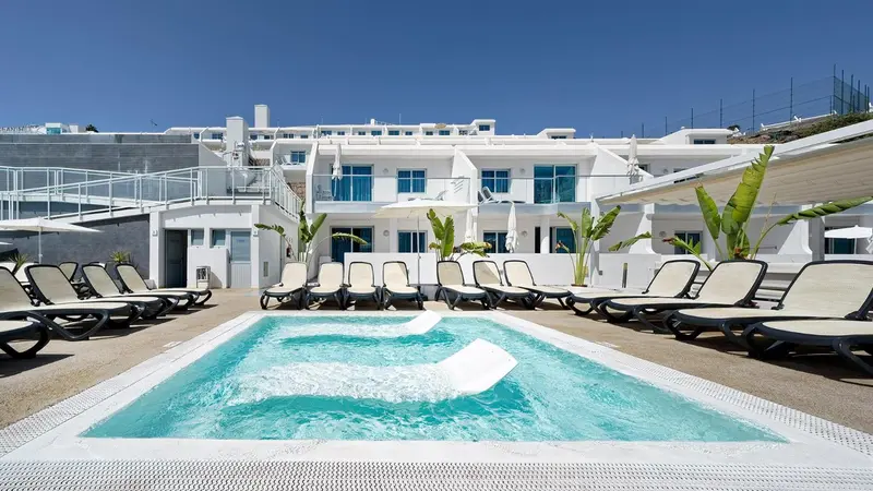Piscine et transats devant un bâtiment blanc.