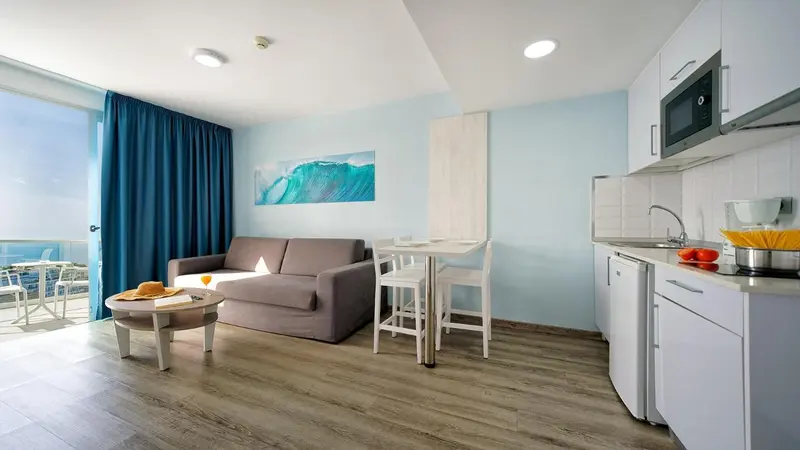 Espace de vie lumineux avec canapé, table et cuisine équipée.