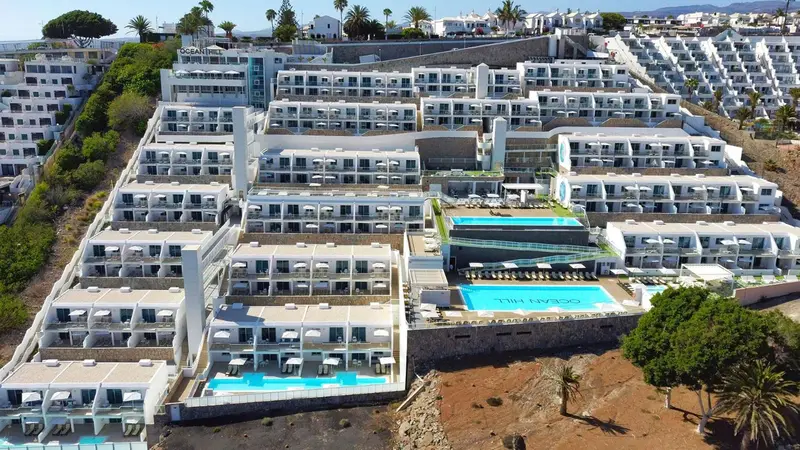 Vue aérienne d'un complexe hôtelier blanc avec plusieurs piscines et terrasses.