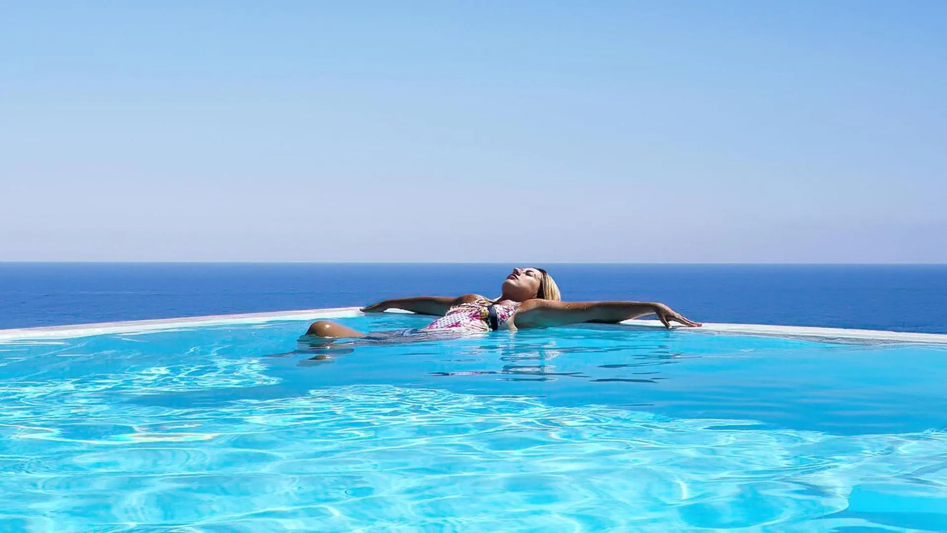 Une femme se détend dans une piscine à débordement avec vue sur la mer.