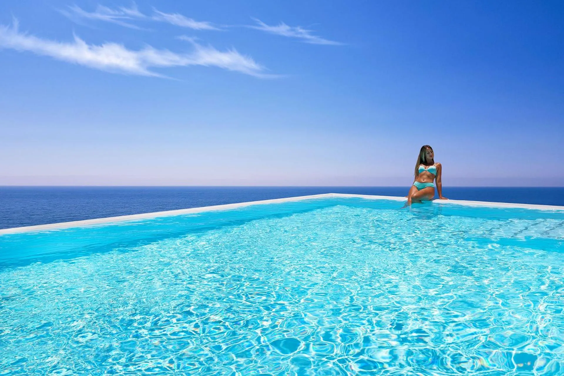 Une femme est assise au bord d'une piscine à débordement avec vue sur la mer.