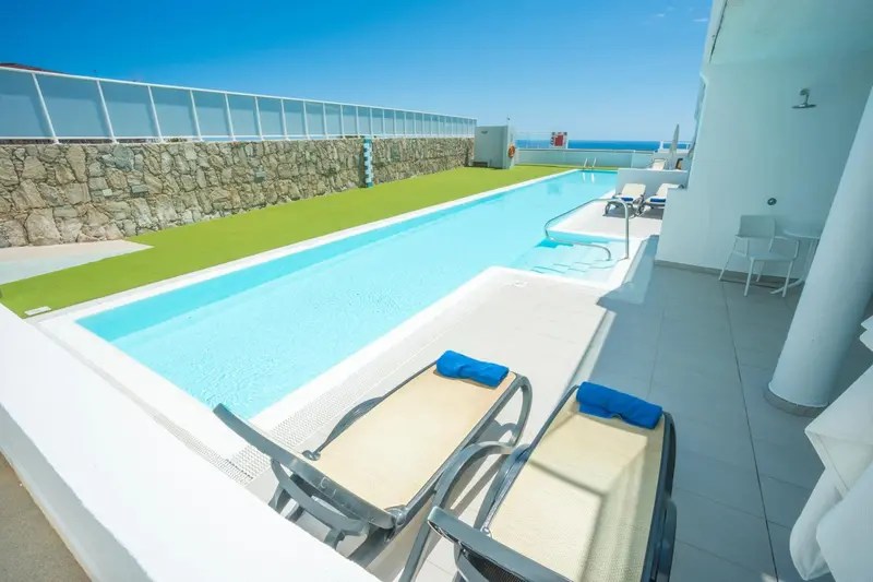 Une piscine rectangulaire avec des transats sur une terrasse ensoleillée.