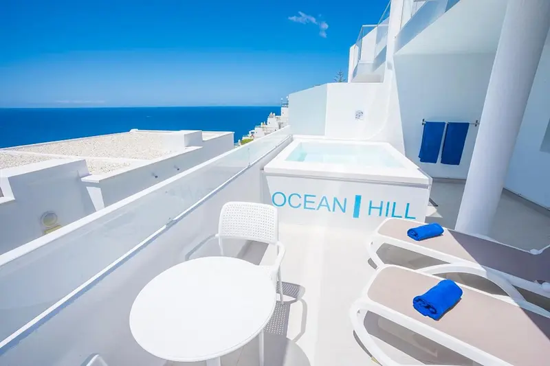 Terrasse avec jacuzzi et mobilier blanc offrant une vue sur la mer.