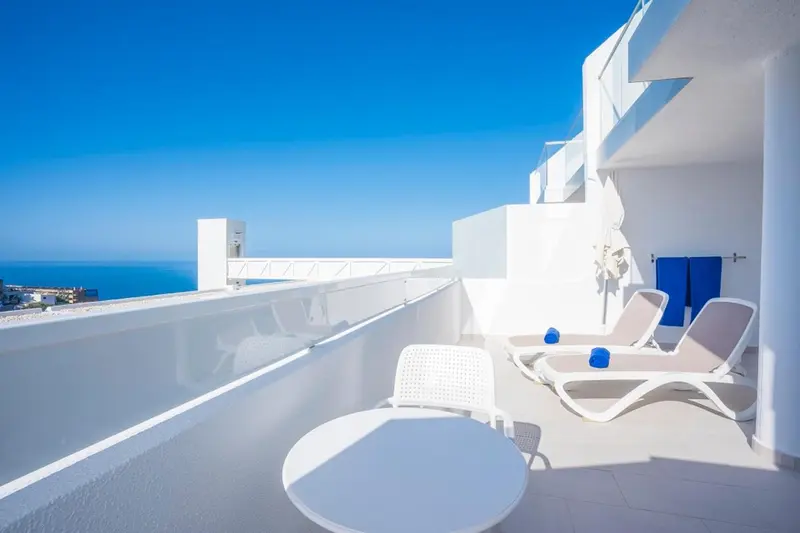 Terrasse blanche avec mobilier d'extérieur et vue sur la mer.