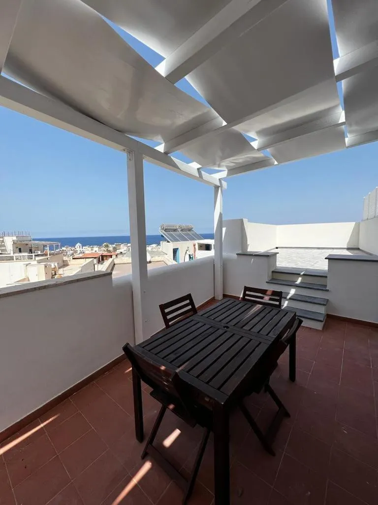 Terrasse ombragée avec table et chaises donnant sur la mer.