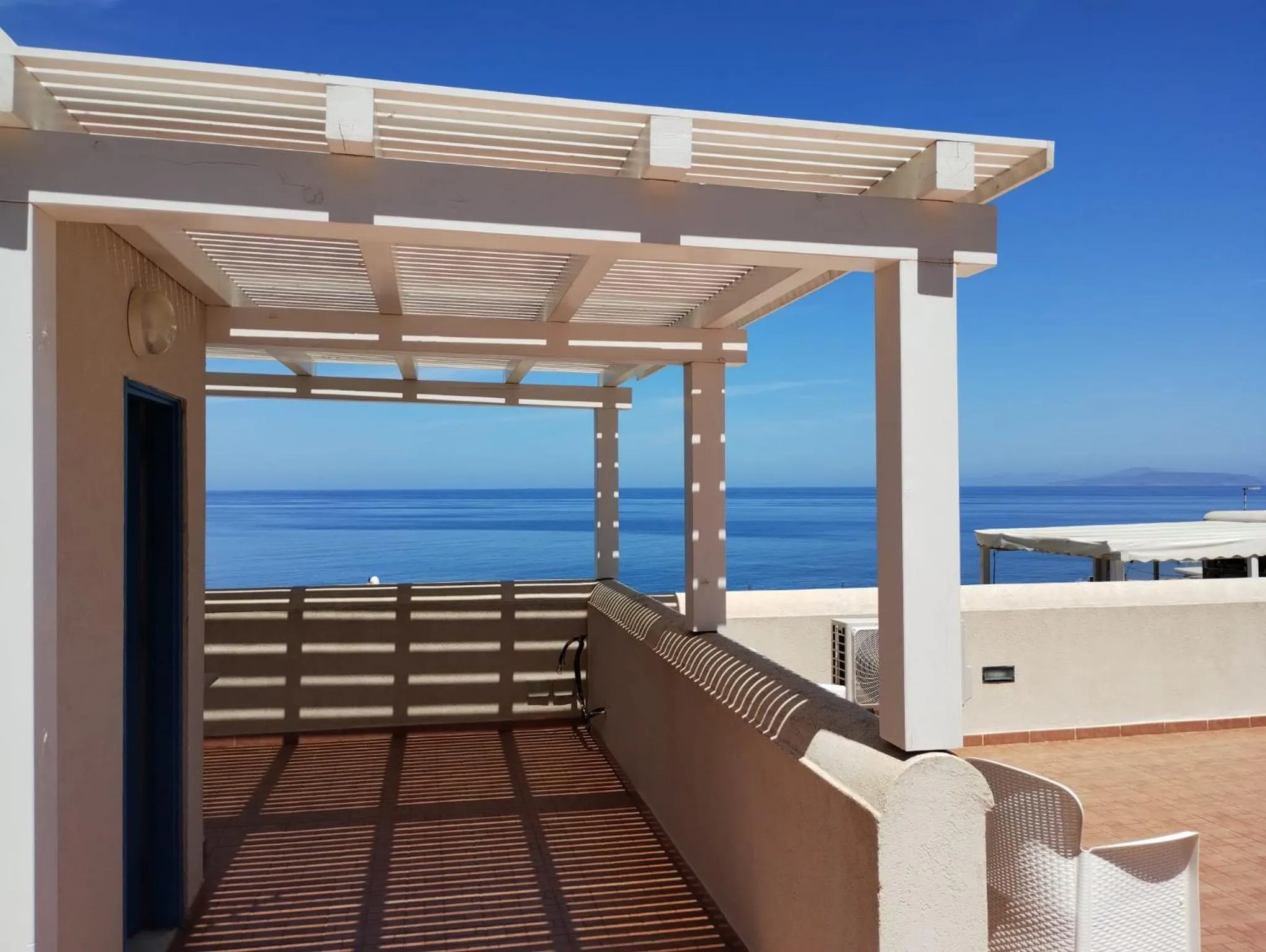 Terrasse ombragée avec vue sur la mer et les montagnes.