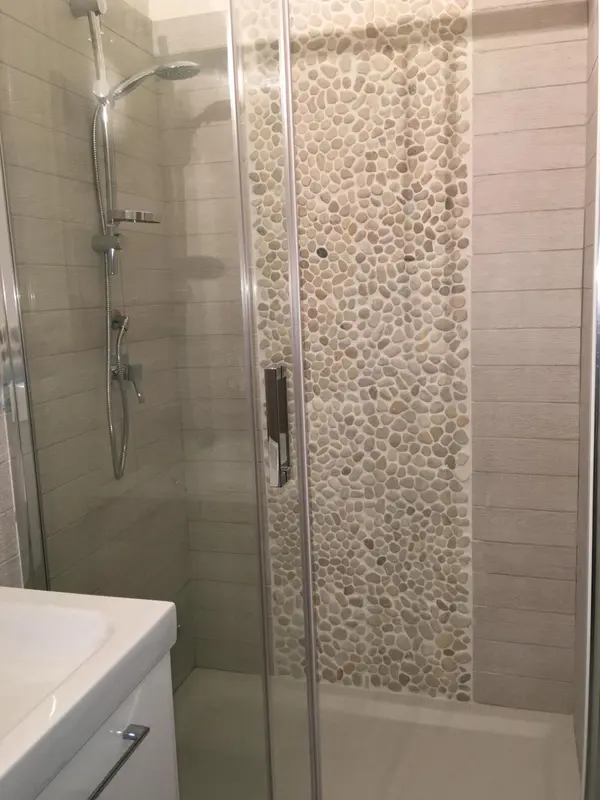 Douche à l'italienne avec paroi en verre et mosaïque de galets.