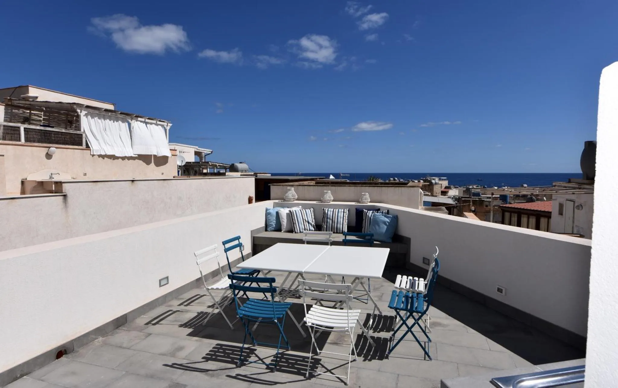 Terrasse aménagée avec table et chaises, vue sur la mer et le ciel bleu.
