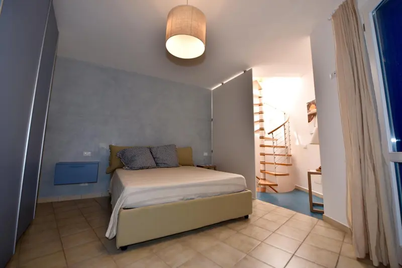 Une chambre lumineuse avec un lit double et un escalier en colimaçon.