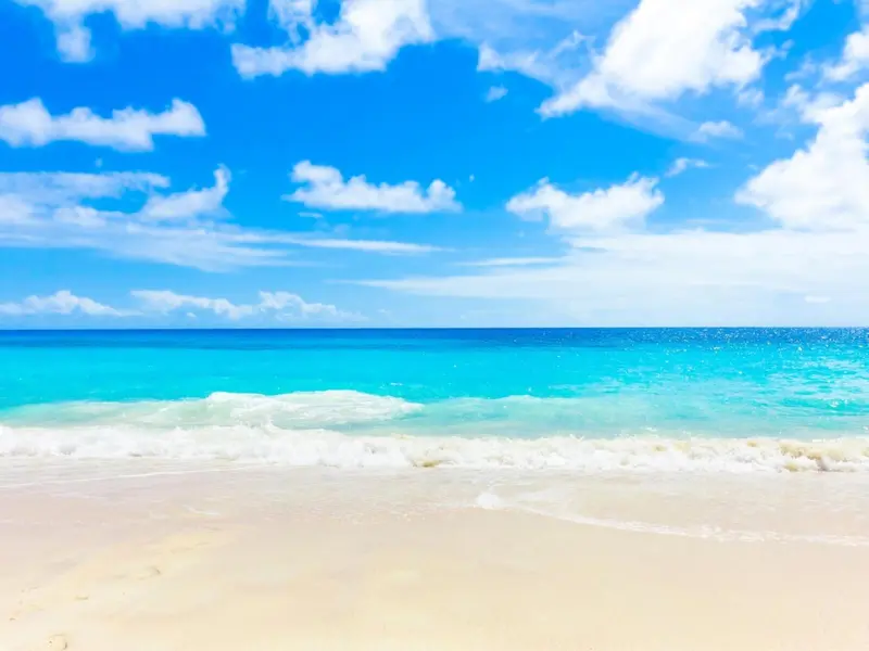 Plage de sable blanc bordée par une mer turquoise sous un ciel nuageux.