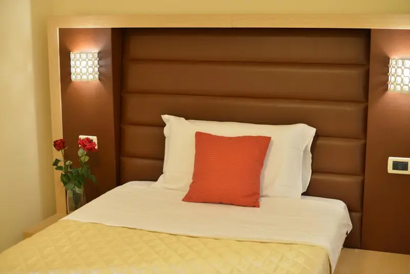 Un lit avec des oreillers et un coussin rouge est devant une tête de lit marron.