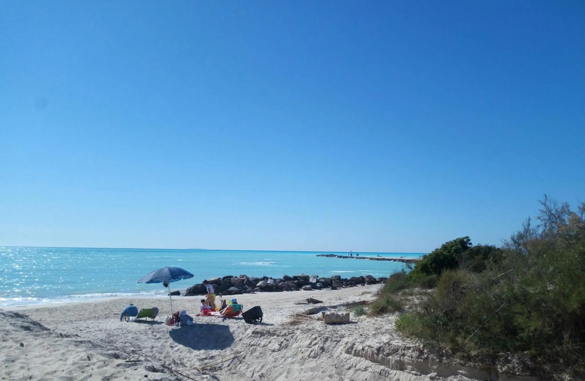 Une plage de sable clair avec des parasols et des personnes assises près de la mer.