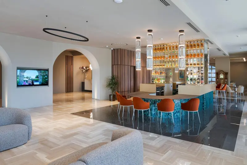 Un bar moderne avec un comptoir turquoise et des tabourets orange dans un espace lumineux.