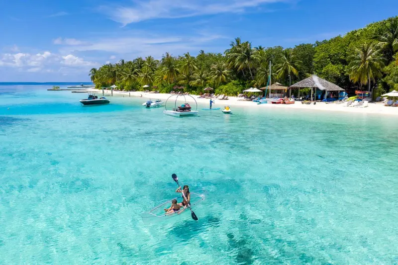 Vue aérienne d'une plage de sable blanc bordée de palmiers et d'une eau turquoise.