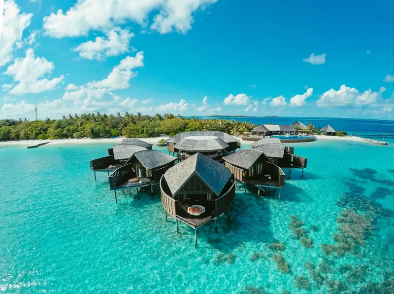 Vue aérienne d'un ensemble de bungalows sur pilotis au-dessus d'une eau turquoise.
