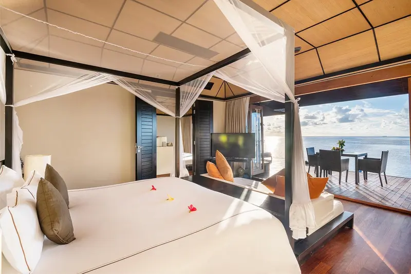 Une chambre lumineuse avec un grand lit à baldaquin donnant sur une terrasse en bord de mer.