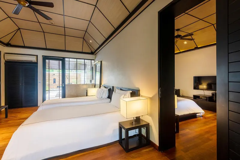 Une chambre lumineuse avec deux lits simples et un ventilateur au plafond.