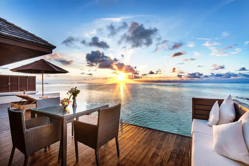 Terrasse en bois avec mobilier de jardin face à l'océan au coucher du soleil.