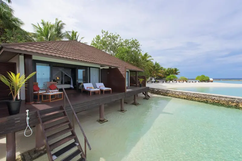 Une terrasse en bois donne sur une plage de sable blanc et une mer turquoise.