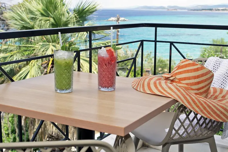 Deux cocktails colorés et un chapeau de paille reposent sur une table en bois sur une terrasse ensoleillée.