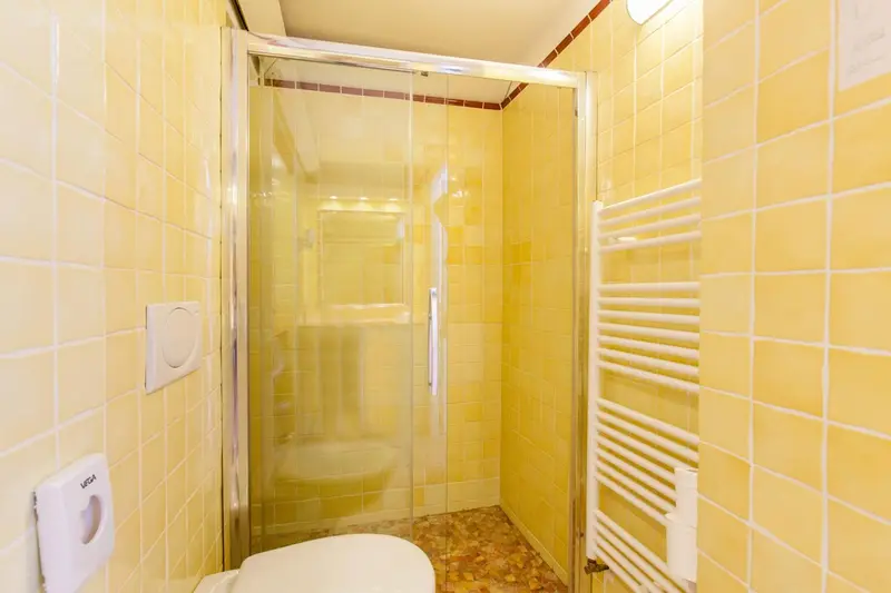 Une salle de bain claire avec douche vitrée et carrelage jaune.