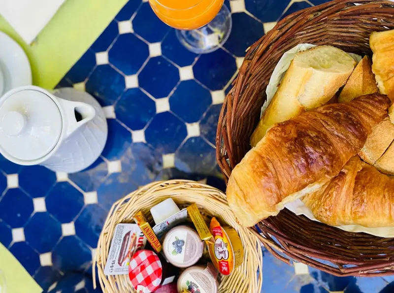 Une table carree bleue et blanche presente un petit-dejeuner avec des viennoiseries et des confitures.