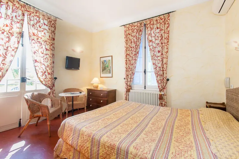 Une chambre lumineuse avec un lit recouvert d'une courtepointe et une petite table avec des chaises.