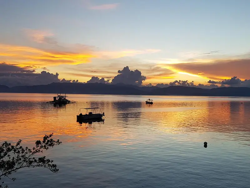 Coucher de soleil sur une mer calme avec quelques embarcations.