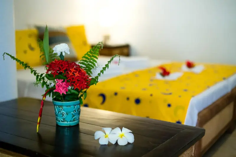 Composition florale colorée sur une table en bois devant un lit décoré.