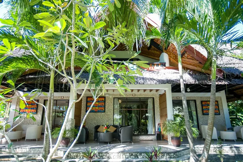 Façade d'un bâtiment avec une terrasse ombragée par des palmiers.