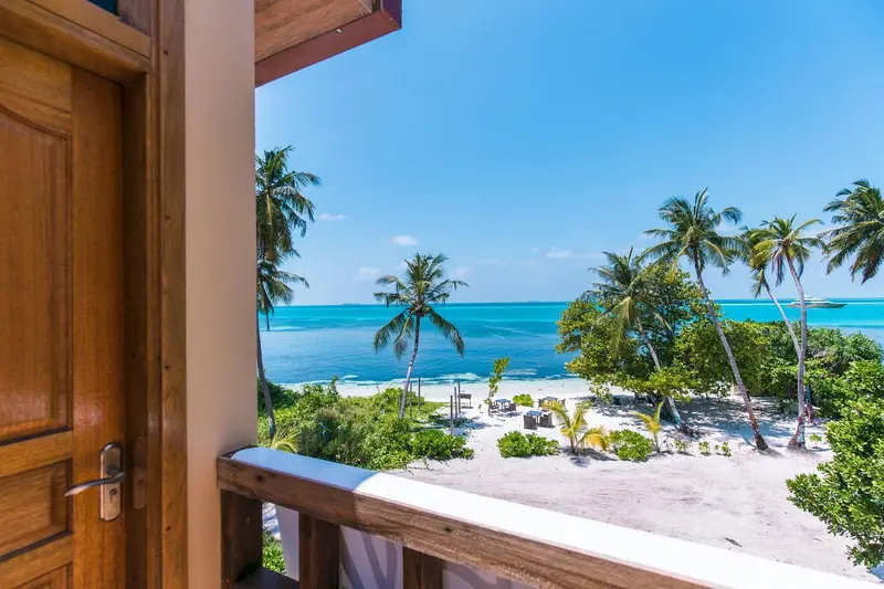 Vue sur une plage de sable blanc bordée de palmiers depuis un balcon.