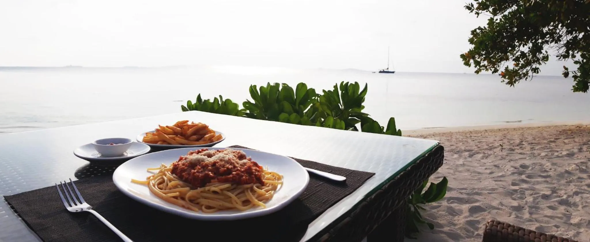 Assiettes de pâtes et de frites sur une table en bord de mer.