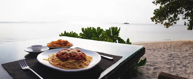 Assiettes de pâtes et de frites sur une table en bord de mer.